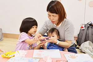 お母さんから手にインクをつけてもらう女の子
