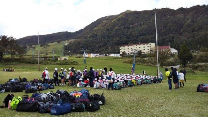 緑豊かな高原で集まって座っている児童たちの写真