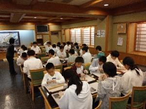 テーブルを囲んで椅子に座り、生八つ橋作り体験をする児童たちの写真