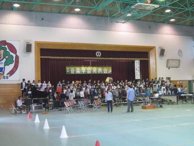 水色の床の体育館で音楽練習をする児童たちの写真