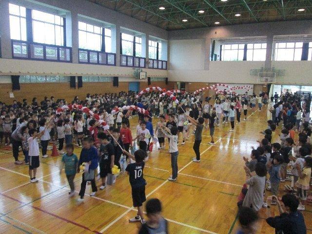体育館で2年生から6年生が作った花のアーチの下をくぐりながら1年生が入場してくる様子の写真