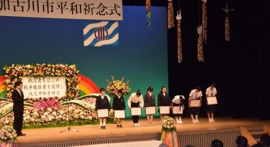 「平和作文コンクール表彰式」の写真。ステージ上に受賞した小・中学生6名が確認できる。