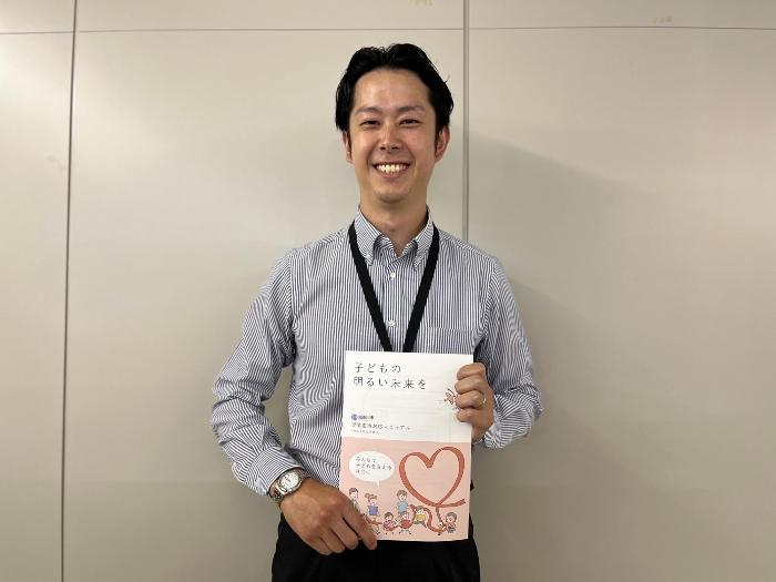 「子どもの明るい未来を」というパンフレットを持つこども部家庭支援課の石井さんの写真