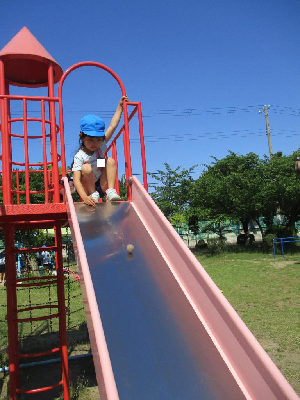 泥だんごを滑り台から転がしてみている5歳児