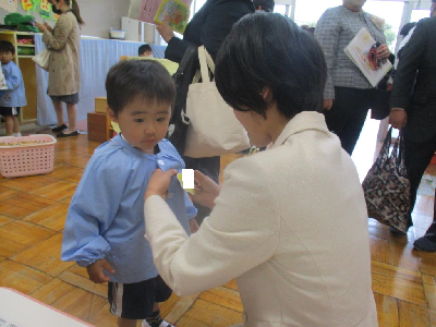 担任に名札をつけてもらう新入園児
