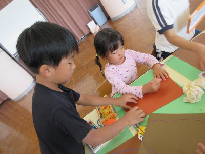 年長児が年少児に制作の仕方を教えてあげる様子