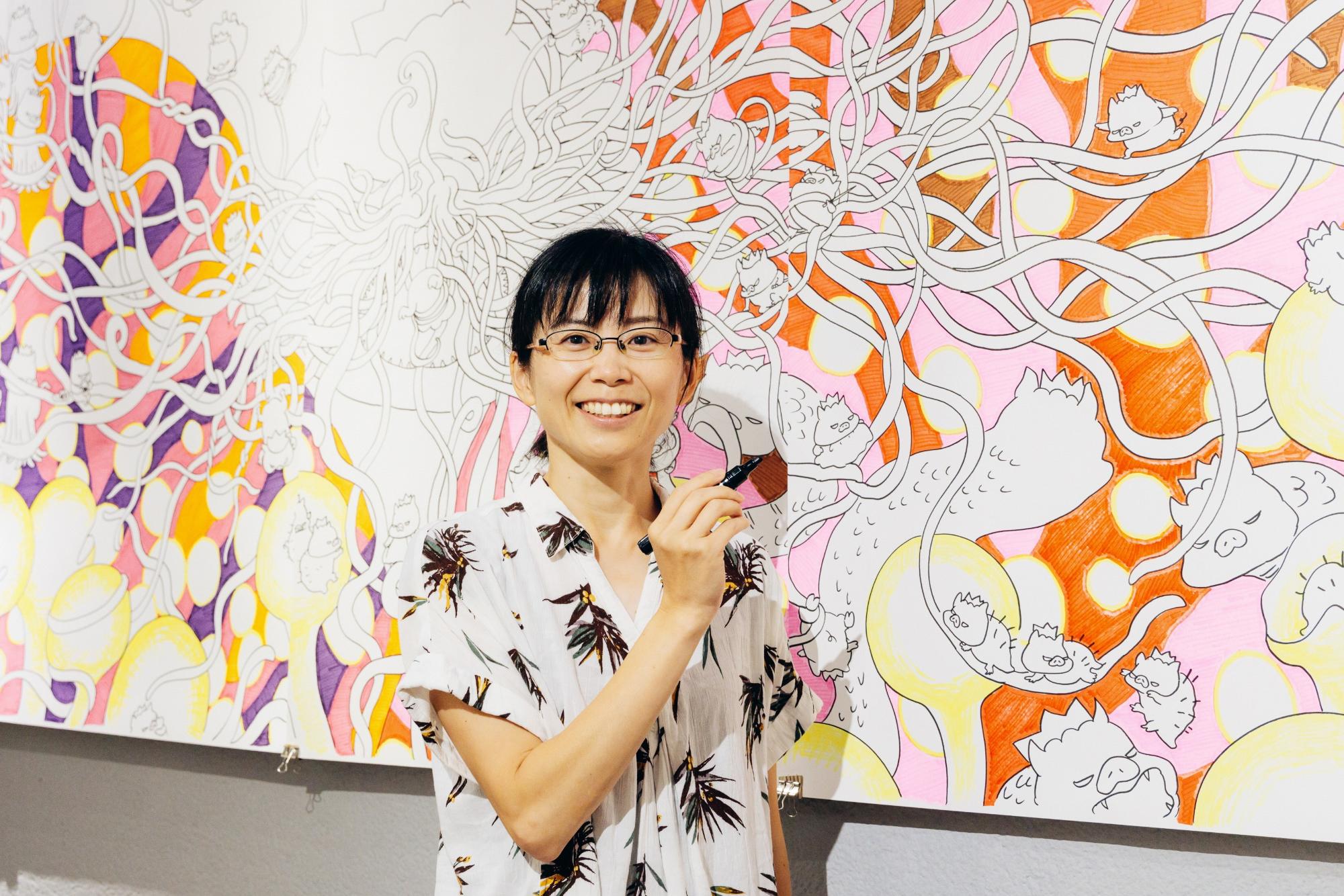 イラストの前に立つ久保田裕美さん