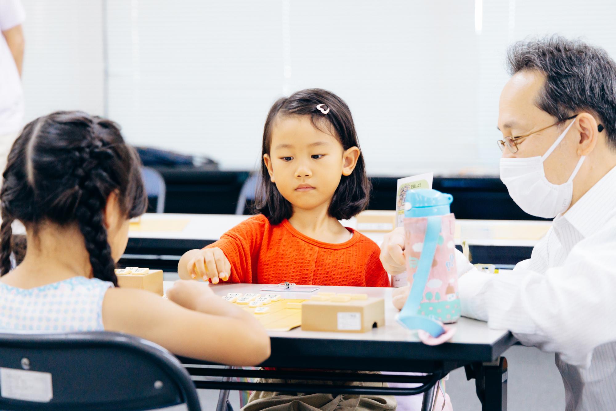将棋教室で先生に将棋を教わる女の子