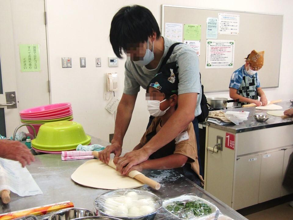 お父さんと一緒に、めんぼうにうどんの生地を巻いている様子