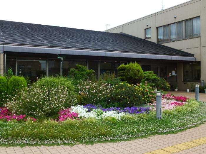 建物前に色とりどりの花が咲いている植え込みがある陵南公民館の外観写真