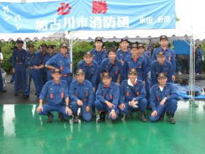 ポンプ操法大会で必勝の旗を背に記念撮影をする加古川市消防団員たちの写真