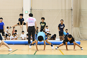 ゴム製のマットを開脚飛びする子どもと手を床についた姿勢で前進する子どもたち