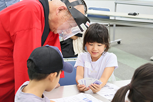 先生からトランプを使ったマジックを教えてもらう女の子
