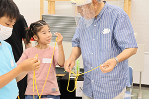 先生からロープを使ったマジックを教えてもらう女の子