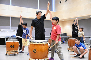 太鼓を打つ手の肘を伸ばすよう指導する先生