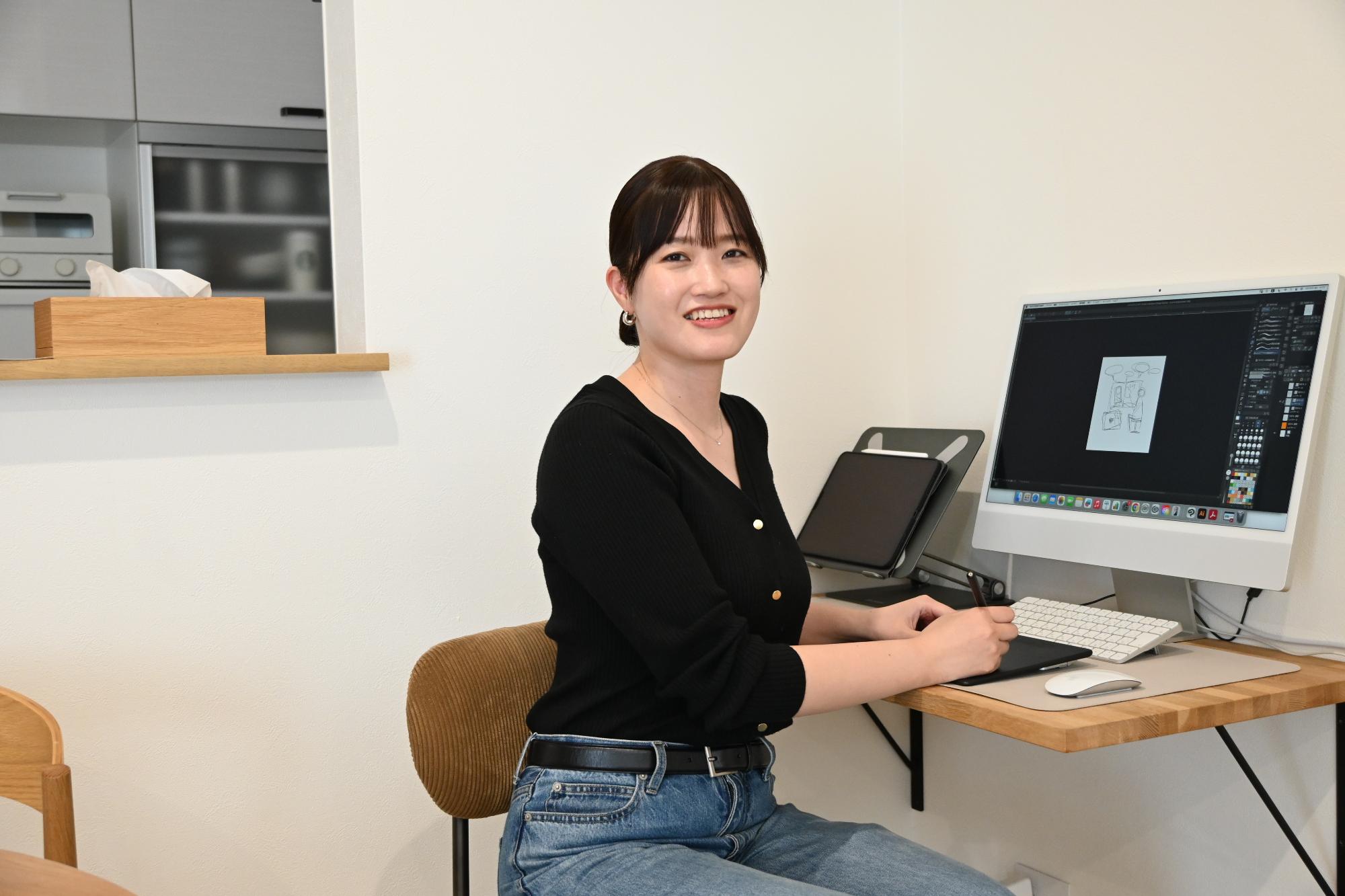イラストを制作するデスクで笑顔を見せるたなかのりこさん