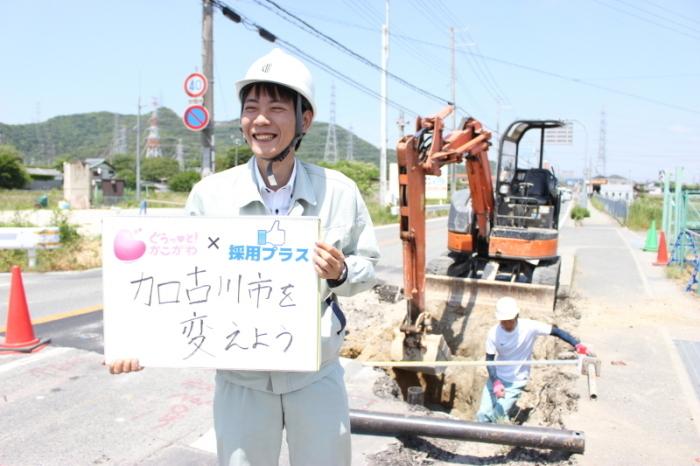 「加古川市を変えよう」と手書きされたスケッチブックを持つ上下水道局下水道課の朝倉さんの写真