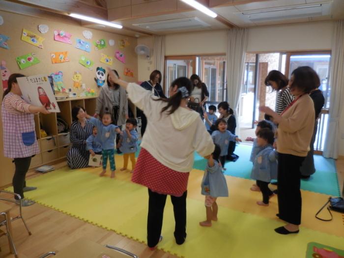 大型絵本の「だるまさんと」を見る園児たちに参観していた父母も混ざる様子の写真