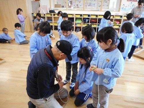 老人会のおじいちゃんにこま回しを教わっている園児の写真