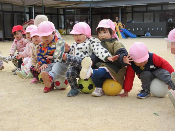 2歳児がボールに座って片足を挙げてバランスをとっている。