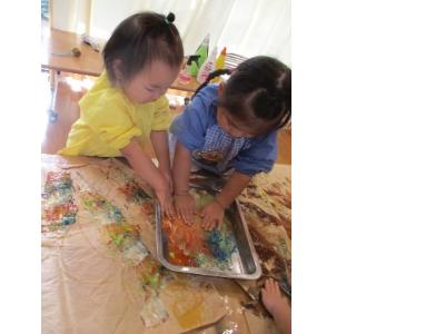 秋の色の絵の具を手で混ぜる2歳児