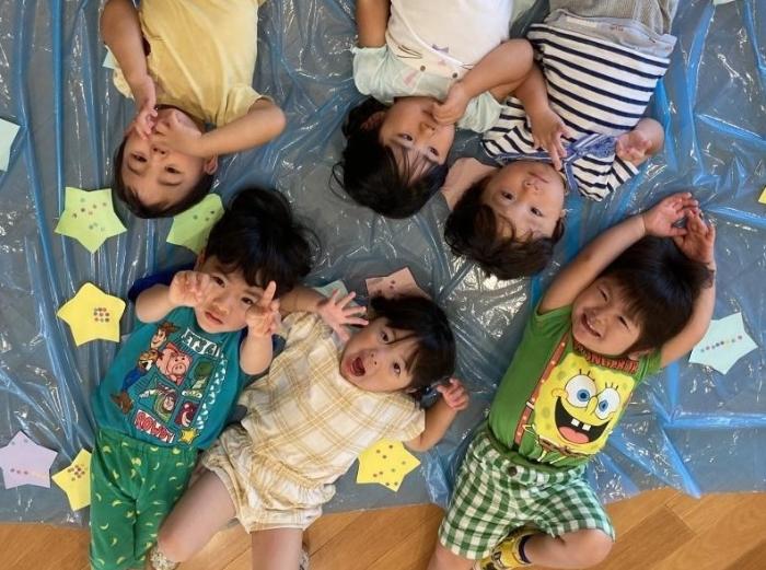 天の川の製作の上で寝ころび笑顔の2歳児