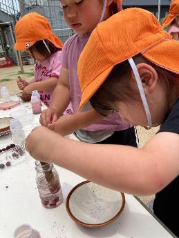 ミニボトルに水とヤマモモ入れ、棒でつぶしジュースを作ろうとする3歳児