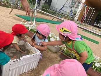 1歳児の友達の顔に泥がついていることを知らせる2歳児