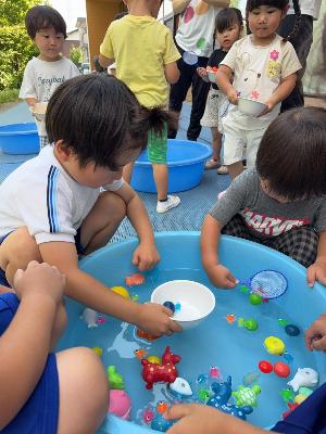 2歳児の金魚すくいを手伝う5歳児