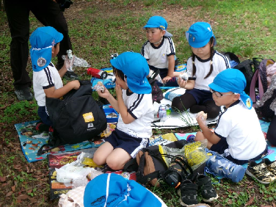 外でみんなでお弁当を食べる年長児