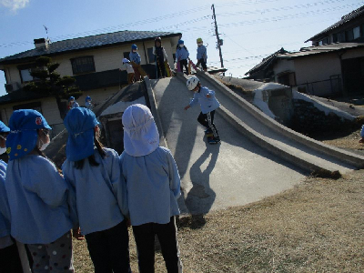 築山でスキージャンプごっこをする園児