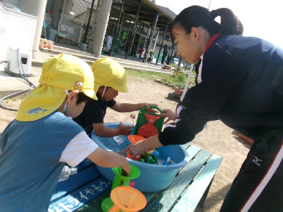 中学生のお姉さんと一緒に水遊びをする年少児