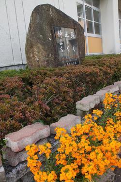 手前に花が咲いている植え込みの中に設置された校訓の碑の写真