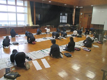 多目的室の床に新聞紙を広げ、児童たちが書き初めを行う様子