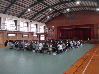 PTA総会の様子。体育館で、多数の保護者が席につき、議題を確認している。