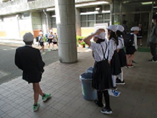 計画委員の児童が、玄関でアルミ缶回収をしながら、あいさつをしている様子。