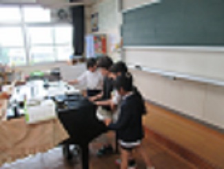 音楽室で、音楽の教師と児童がピアノを弾いている。