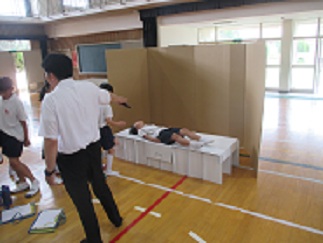 避難所で使われる簡易ベッドに、児童が寝転んでみている。