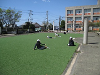 晴れの日の休み時間の様子。芝生の上で児童が座ったり寝転んだりしている。