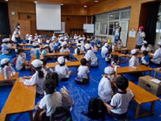 多目的室に集まった5年生と保育園の子たちが、教師の説明を聞いている。