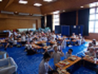 多目的室全景。5年生と保育園の子が一緒に給食を食べている。