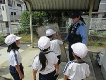交番で、児童が警察官の使う盾を持たせてもらっている様子。