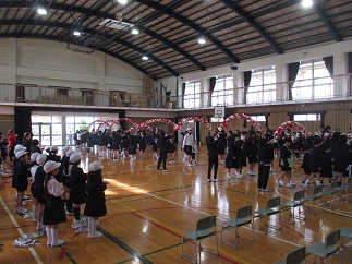 1年生を迎える会で、6年生に連れられた1年生が、花のアーチをくぐって体育館に入場している。