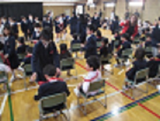 1年生を迎える会で、2年生から5年生までが作ったプレゼントのポシェットを、5年生が代表して渡している。