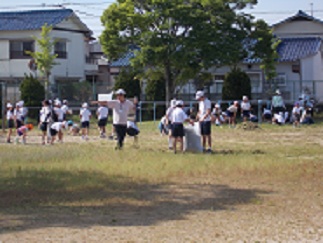 児童と教師、保護者が、刈った草や抜いた草を集めている。