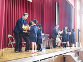 離任式の様子。西神吉小を去る職員に、児童が花束を渡している。