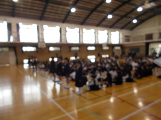 体育館で選任式をしている様子。各学級の学級委員が呼ばれ、立っている。