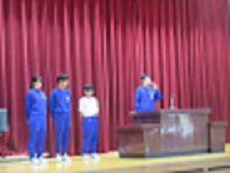 全校朝会で、トライやるの中学生が体育館の壇上の講演台で自己紹介をしている様子。