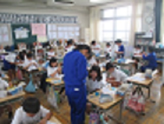 4年生の教室で、中学生が理科の実験キットを作る児童の手助けをしている。