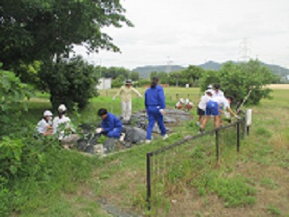 学級園で、中学生が児童と一緒に草を抜いている。